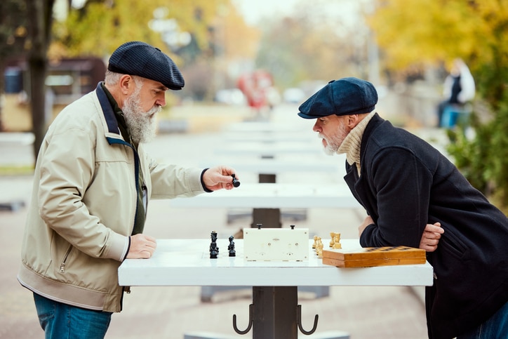 Portrait of two senior men playing chess in the park on a daytime in fall. Warm day walk. Concept of leisure activity, friendship, sport, autumn season, game, entertainment, old generation